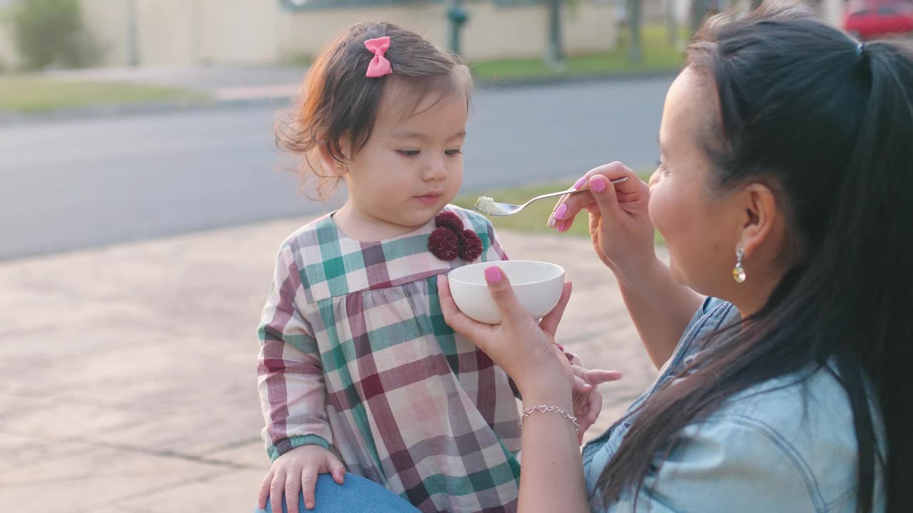 亚洲母亲在前院喂养她的混合蹒跚学步的女儿，家庭生活理念视频素材