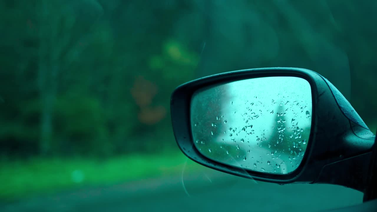 特写，在秋雨天驾驶汽车的侧后视镜。汽车后视镜上的水滴。有选择性的重点。乘汽车旅行。20、绿树青葱，乌云笼罩灰路视频素材