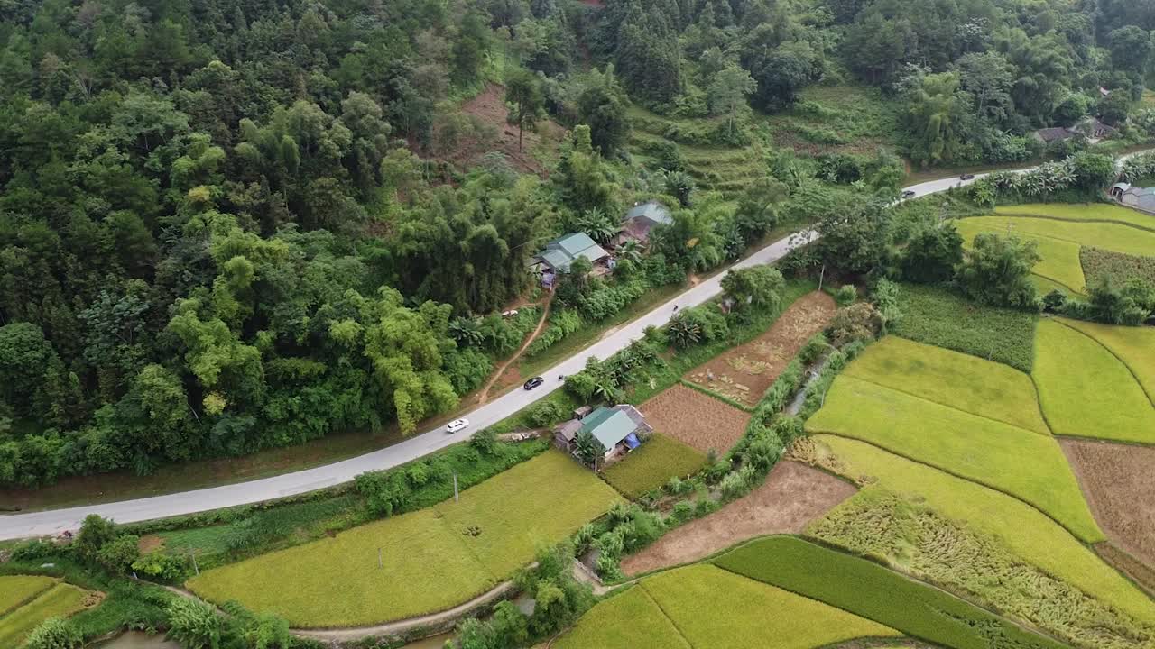 鸟瞰图的道路，汽车和摩托车正在驾驶，在山周围的森林，一个美丽的岩石和稻田的观点视频素材