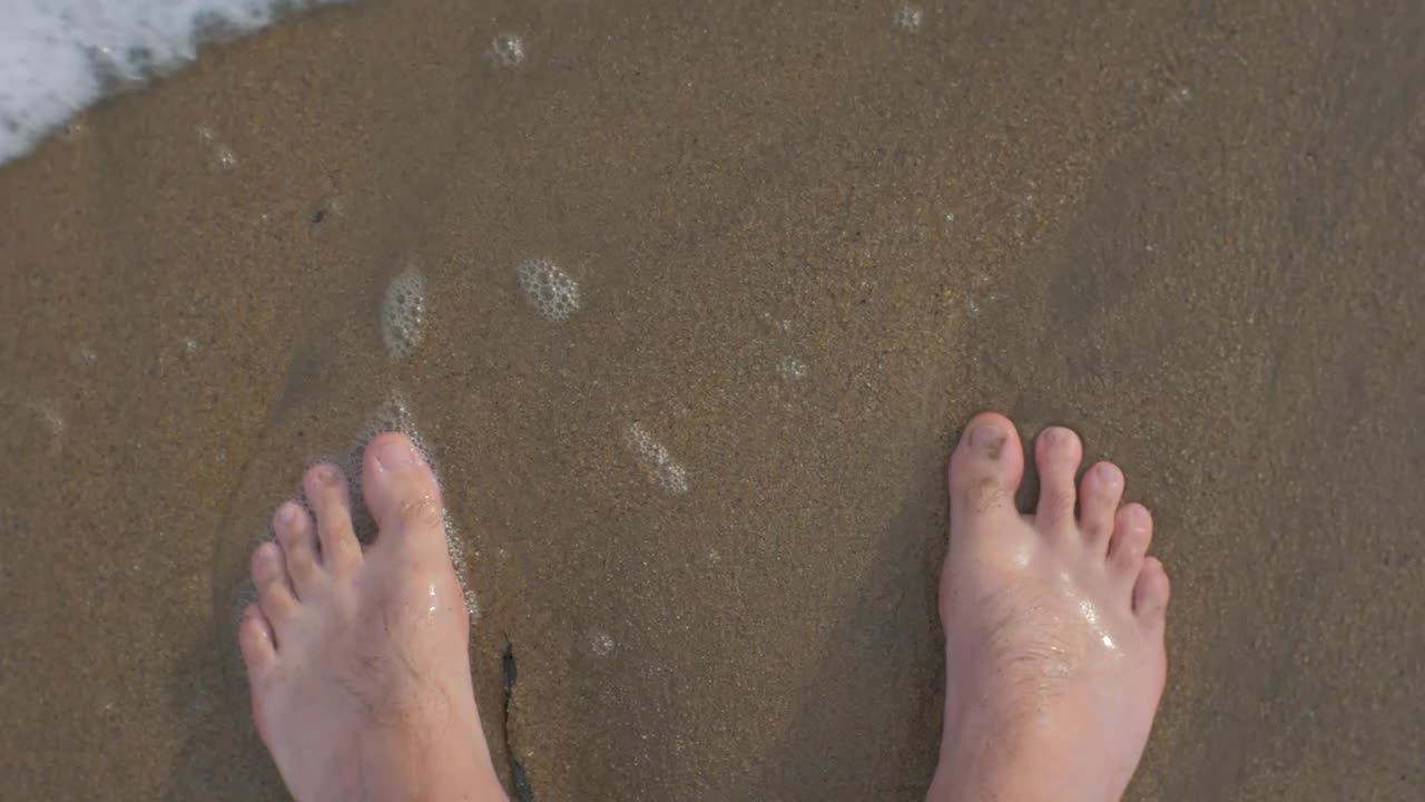 男人光着脚在沙滩上踩进海浪的角度视频素材