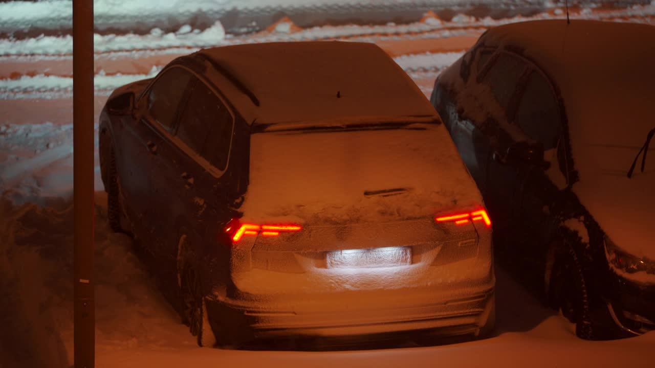 冬天，停车场的路灯下停着的汽车在黄昏时被雪覆盖。城市街道上的大雪。视频素材