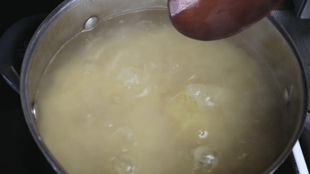 烹饪意大利面的过程中，厨师用木勺混合食物，特写。炉子上的平底锅里的水沸腾了，热气从食物中升起视频素材