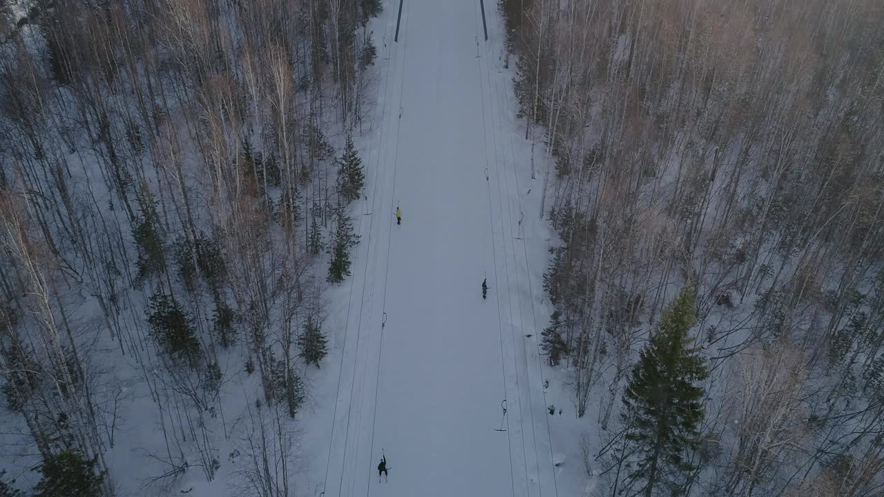 空中倾斜全景图移动的滑雪升降机之间的树木在冬天。乘滑雪缆车上山的滑雪者视频素材