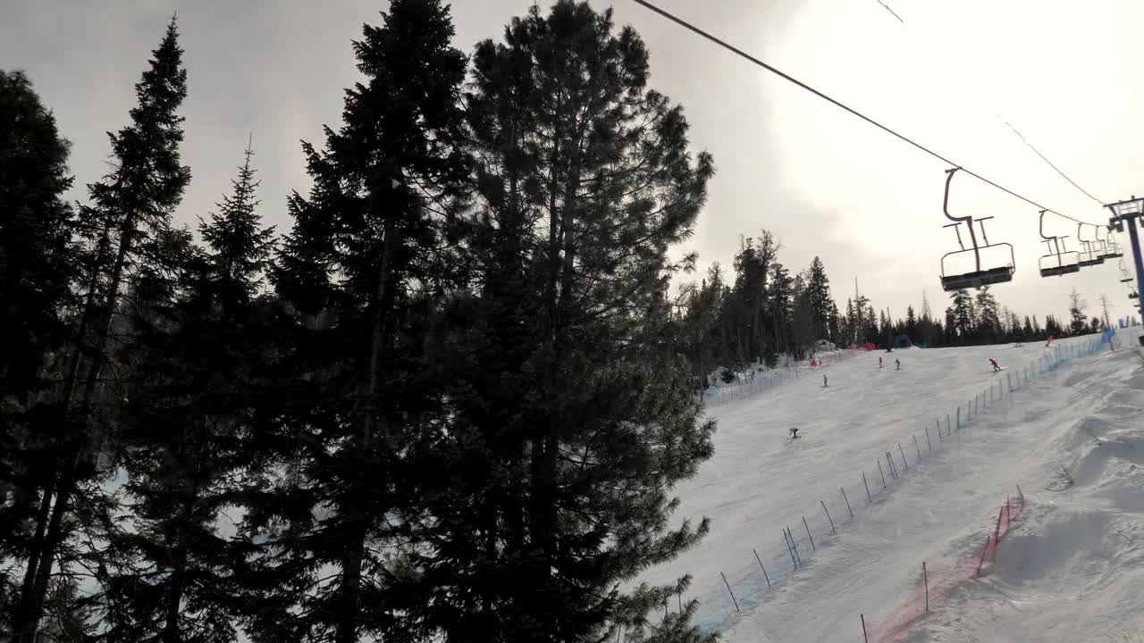 在晴朗的日子里，滑雪缆车索道在树木之间的斜坡上缓缓移动。下山的滑雪者视频素材