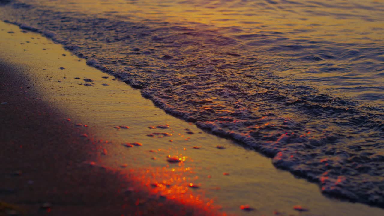 在金色夕阳的傍晚，温暖的海水拍打着黑色的沙滩。海浪视频素材