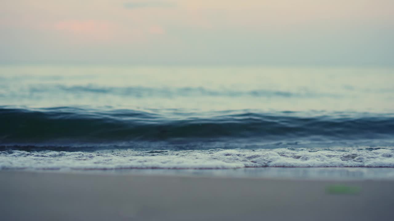 特写蓝色的海浪拍打着海岸线，沙滩在粉红色的天空中慢动作视频素材