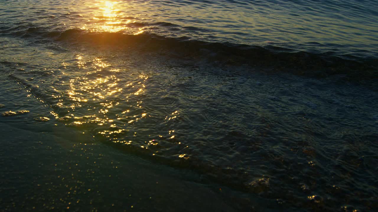 特写平静的海浪在日出的早晨溅起沙滩沙子。蓝色的海浪视频素材