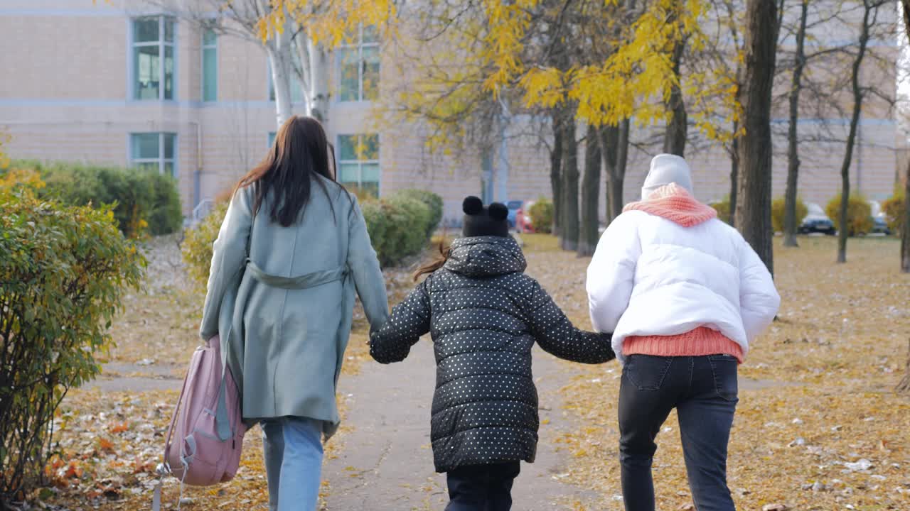 一个女人带着两个女儿匆匆去学校，从后面看到女孩们和她们的母亲沿着秋天的小巷奔跑。视频素材