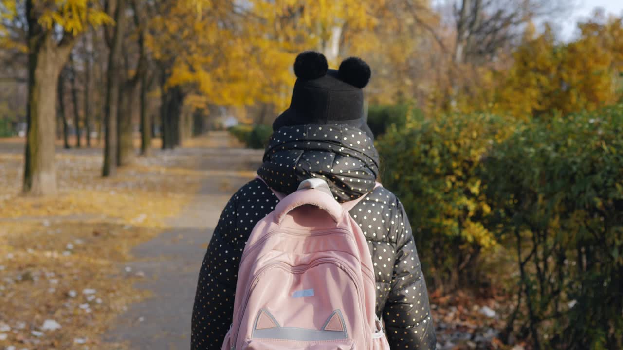 在一个秋天的公园里，从一个小学生上学的小女孩的身后看到的景象。视频下载