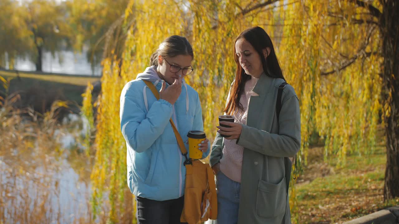 一个女人和她十几岁的女儿在秋天的公园里喝咖啡视频素材