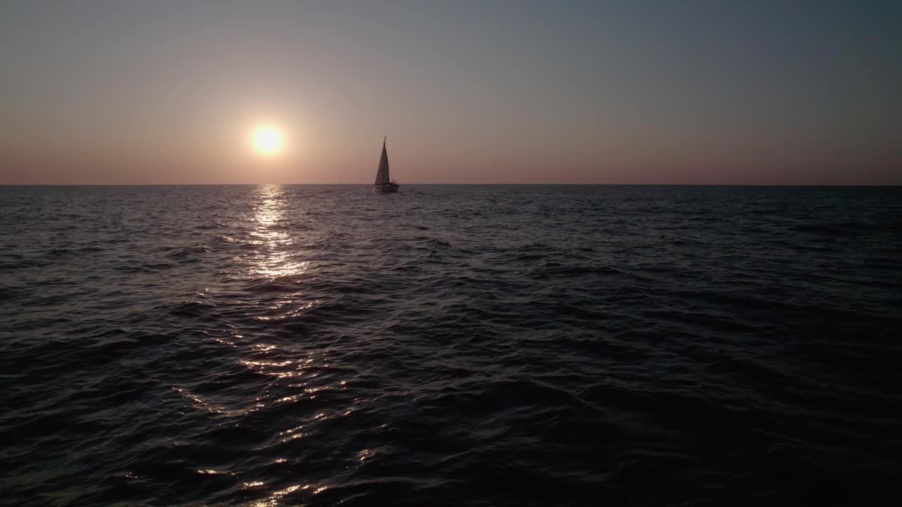 日出在海上，镜头掠过水面。一艘帆船慢慢地迎着天空航行。视频素材