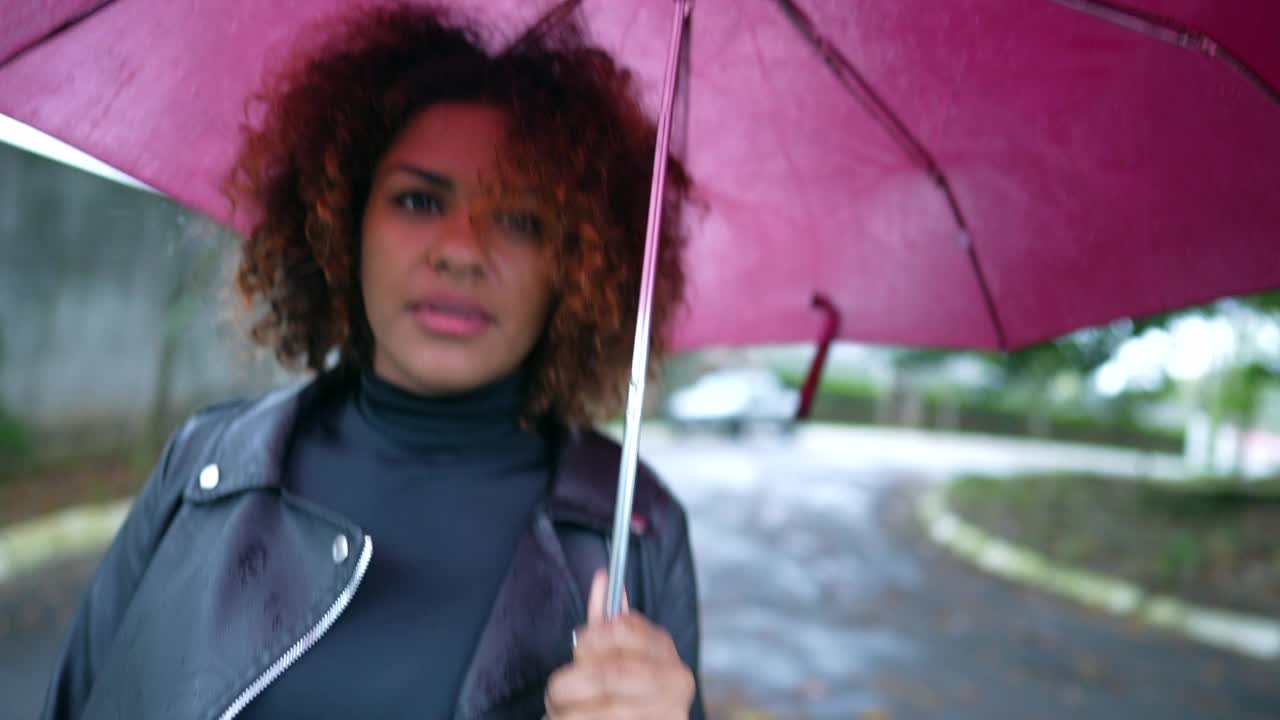 巴西妇女撑着伞在雨中走在城市外面视频素材