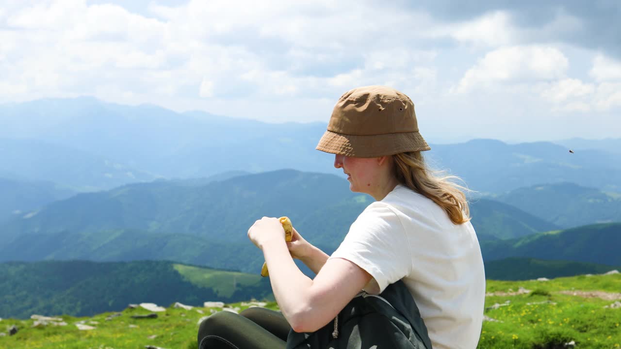 快乐的旅行者探险家女孩吃香蕉水果放松在一个阳光明媚的夏日的山顶视频素材