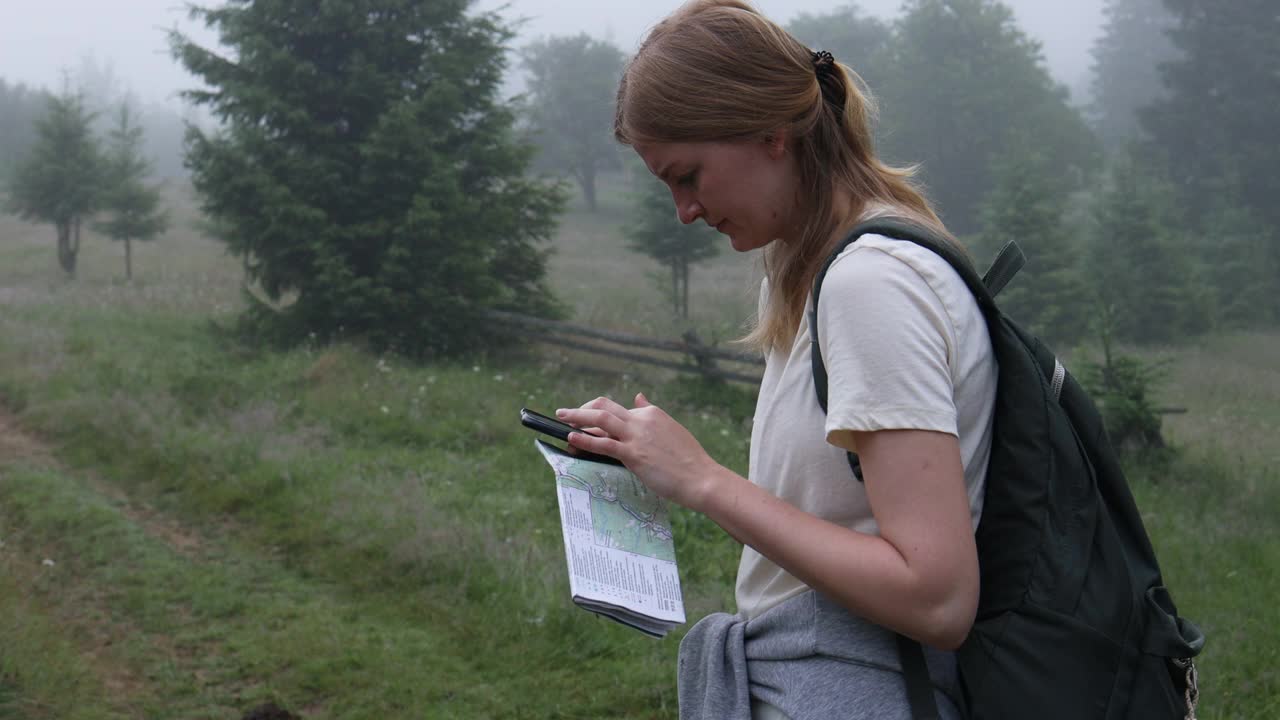 手持地图和智能手机的少女游客正在寻找通往山顶的道路视频素材