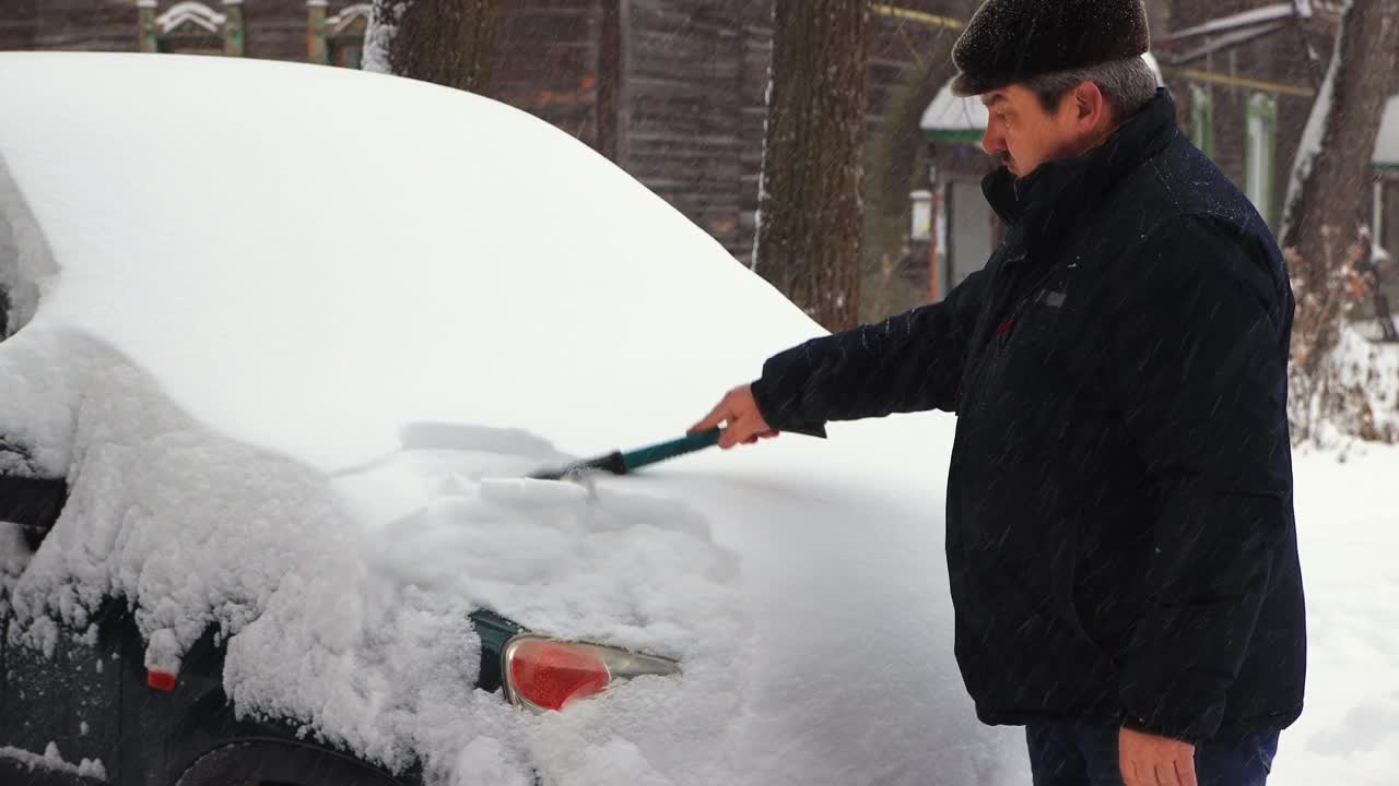 一个人用刷子和刮刀清理他车上的雪。视频素材