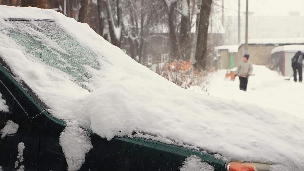 一个男人用刷子清理汽车引擎盖和挡风玻璃上的雪。视频素材