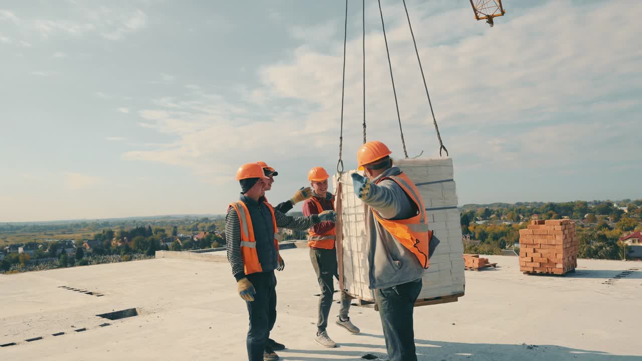 男建筑工在房顶上取砖。建造一座多层红砖房。一辆建筑起重机将砖块运送到屋顶视频素材