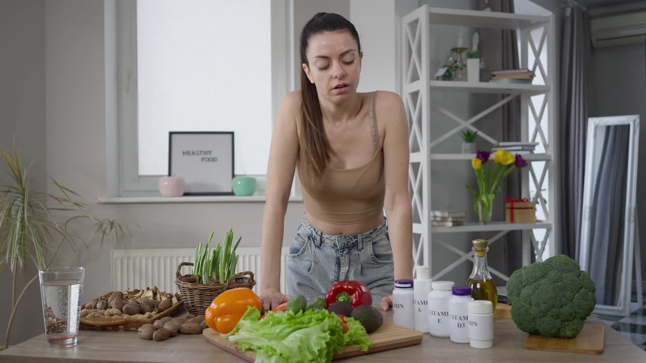 肖像的苗条周到素食妇女站在餐桌选择维生素。苗条美丽的高加索千禧素食女士照顾健康在家室内。健康的饮食和生活方式。视频素材