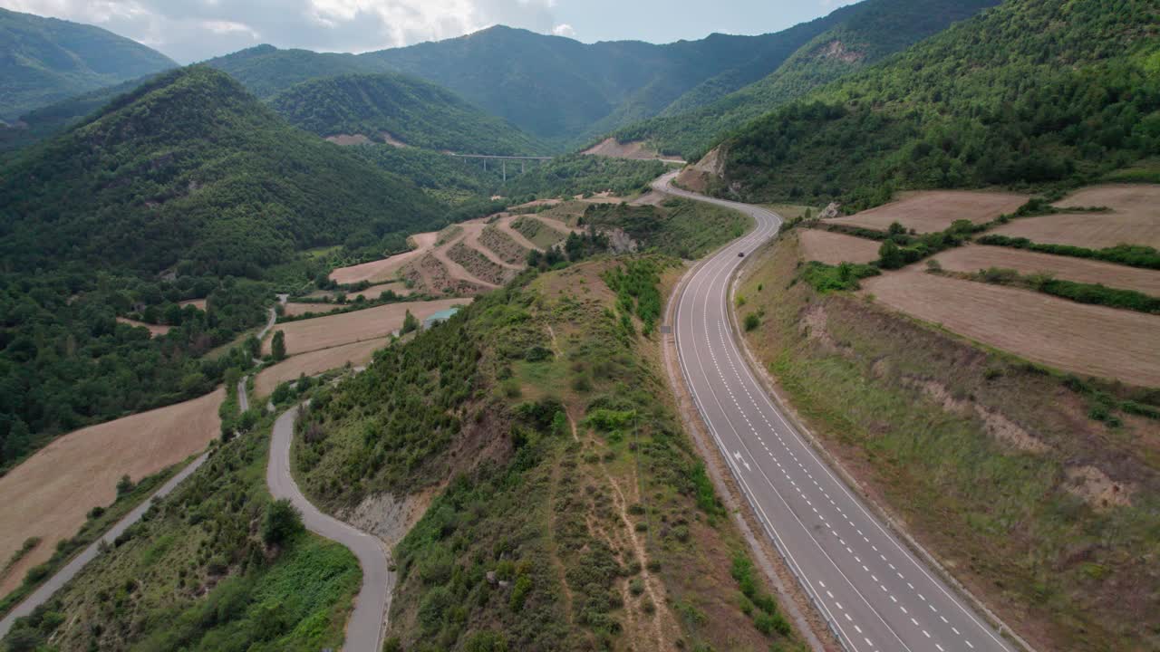 无人机拍摄的高山上柏油路的美景。山脉消失在天空中，天空略多云，但山峰被太阳照亮。视频素材