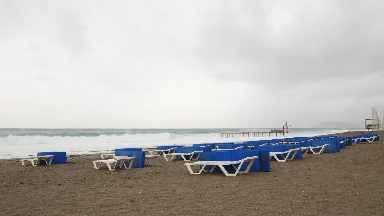 在狂风暴雨的日子里，空荡荡的沙滩和日光浴床。惊涛骇浪的大海。冬天的海岸线空无一人。旅游目的地及度假村视频素材