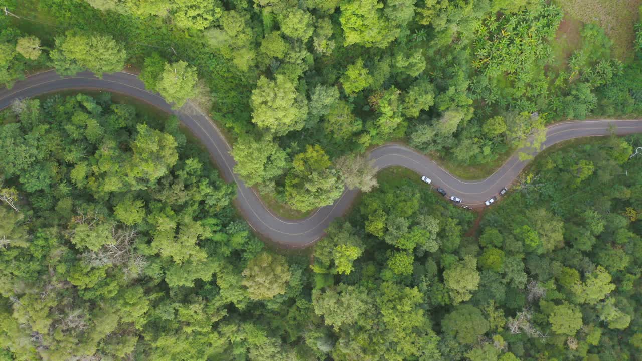 鸟瞰图上的汽车行驶在弯曲，曲折曲线的道路或街道上的山与绿色的天然森林树木在农村地区的南，泰国。交通工具。视频素材