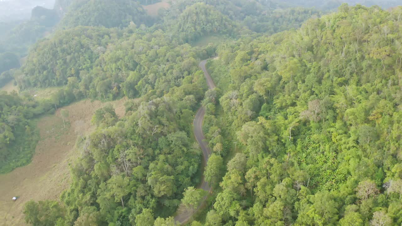 鸟瞰图上的汽车行驶在弯曲，曲折曲线的道路或街道上的山与绿色的天然森林树木在农村地区的南，泰国。交通工具。视频素材