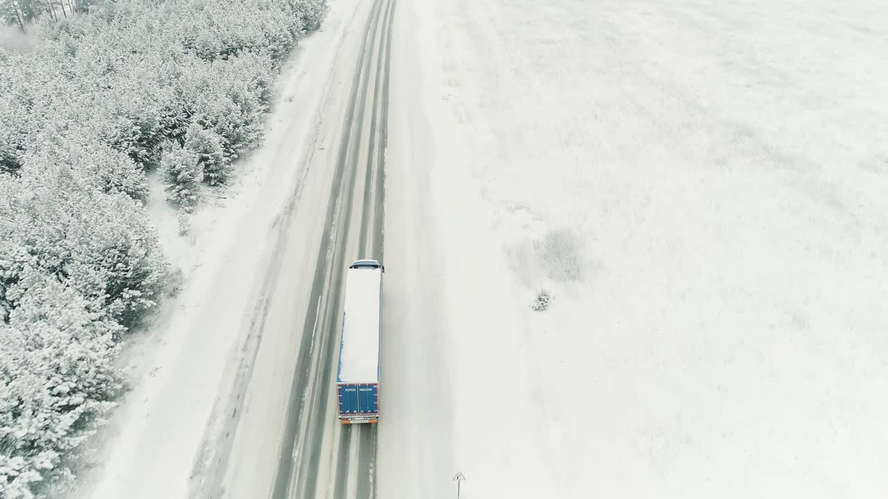 鸟瞰图，一辆伐木卡车行驶在一条穿越云杉林的空旷道路上。现场。交通概念，一辆卡车沿着冰雪覆盖的冬季自然行驶视频素材