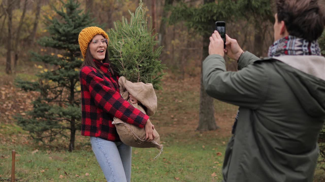 小男孩正在给他的女朋友和新的圣诞树拍照视频素材