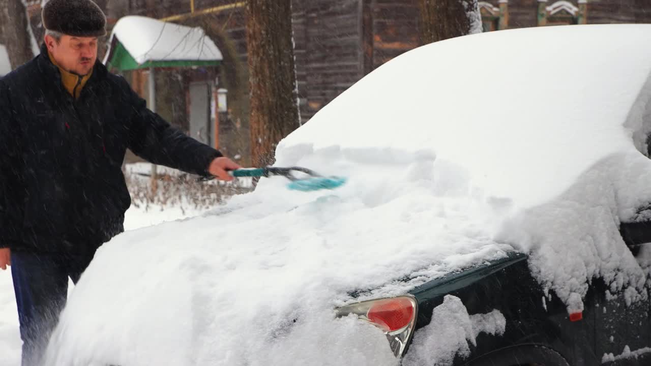 一个男人用刷子清理汽车引擎盖上的积雪。视频素材