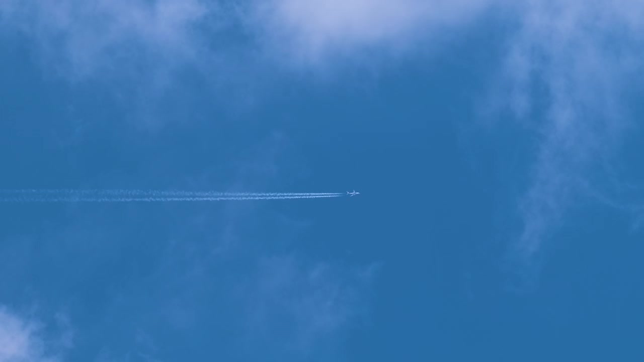 远处的喷气式客机在蓝天上的高空飞行，白云留下烟雾的痕迹。空中旅行的概念视频素材