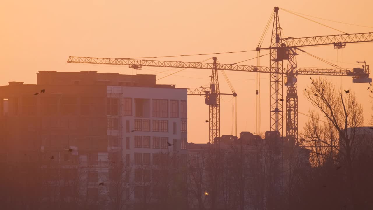 日落时分，高层住宅建筑施工现场塔式起重机的黑色轮廓。房地产开发视频素材