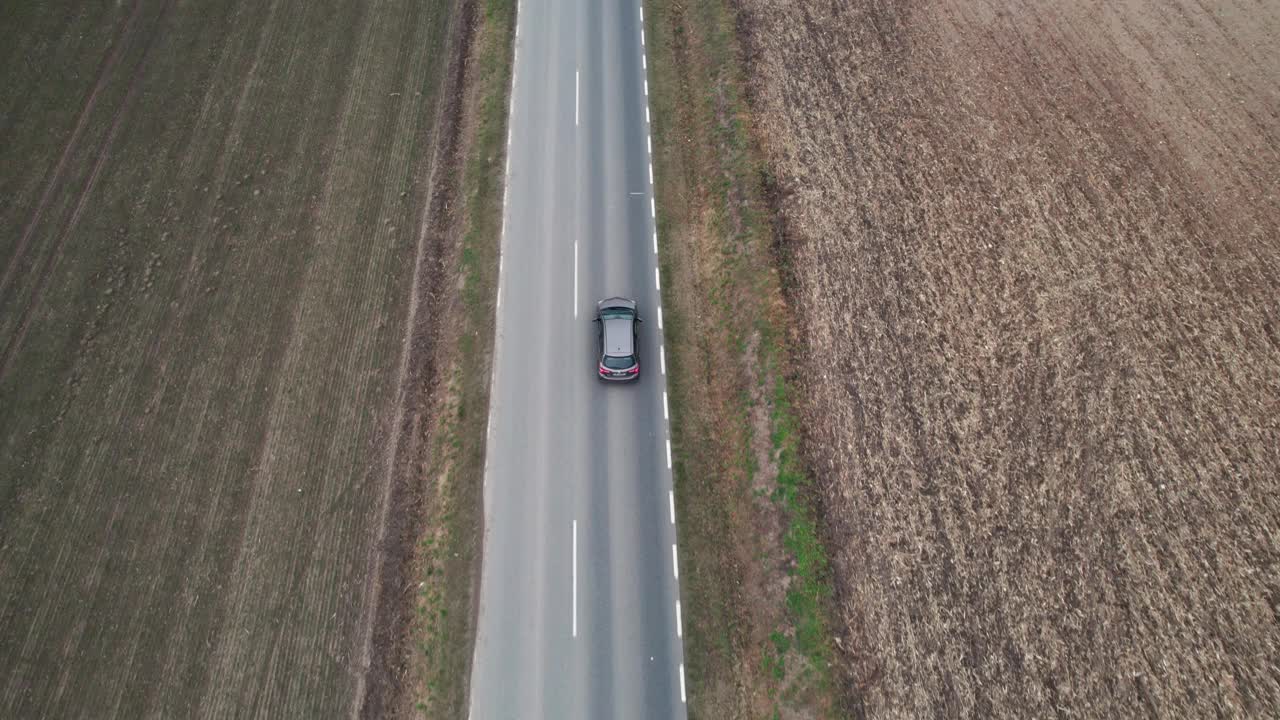 这辆车正行驶在穿过田野的道路上，无人机拍摄了航拍画面。秋天的时候在柏油路上，摄影机跟在车的后面。视频素材