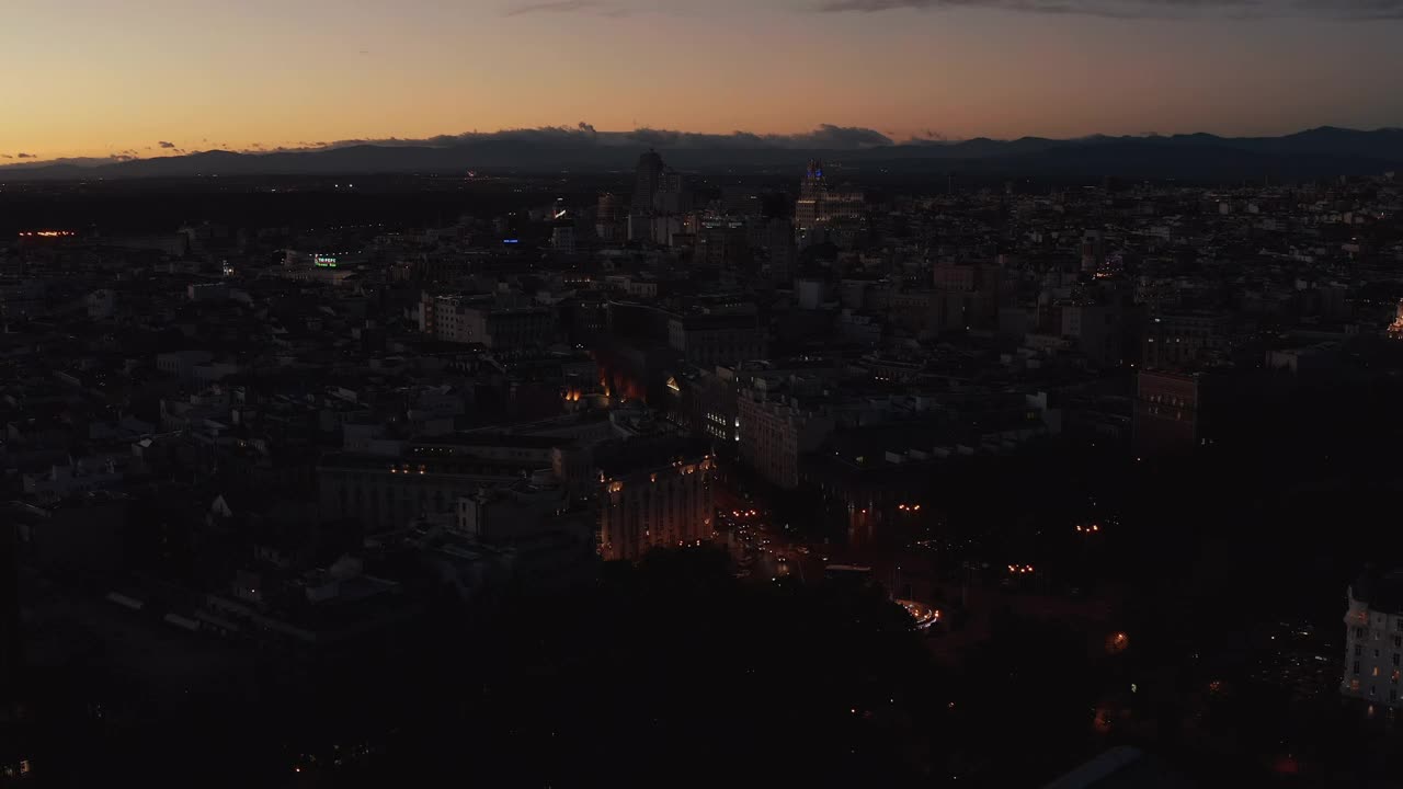 在夜晚的城市上空飞翔。在五彩缤纷的黄昏天空下暗淡城镇的全景鸟瞰图视频素材