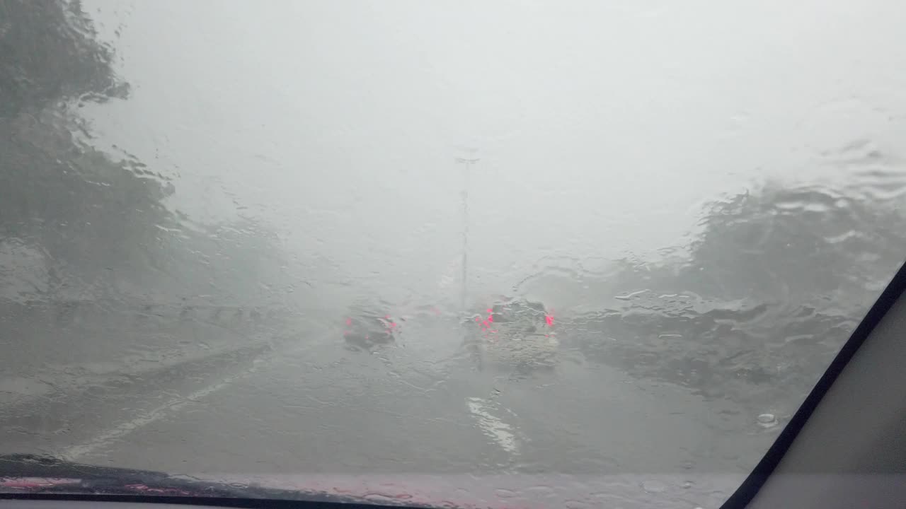 雨滴落在汽车玻璃上。汽车冒着大雨在潮湿的道路上行驶。视频素材