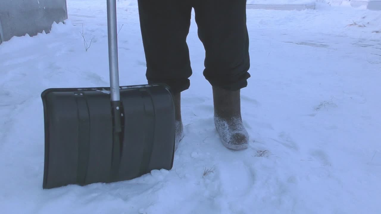 一个人拿着铁锹在晚上清除街道上的积雪视频素材