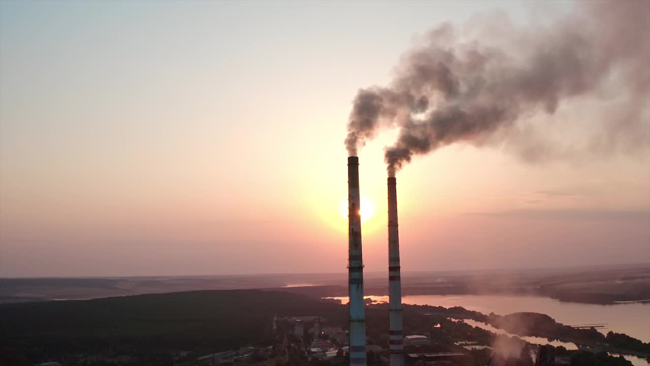 工厂里的大烟筒在夕阳下吸烟。巨大的工业生态雾霾建筑。视频素材