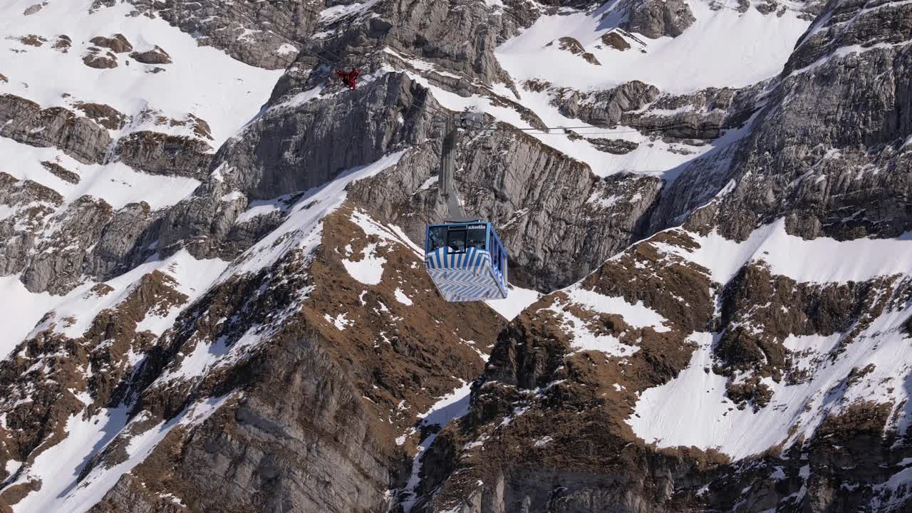 蓝白säntis缆车在下山的路上，在背景中你可以看到白雪覆盖的山，游客们都在小木屋里，白天，阳光灿烂视频下载