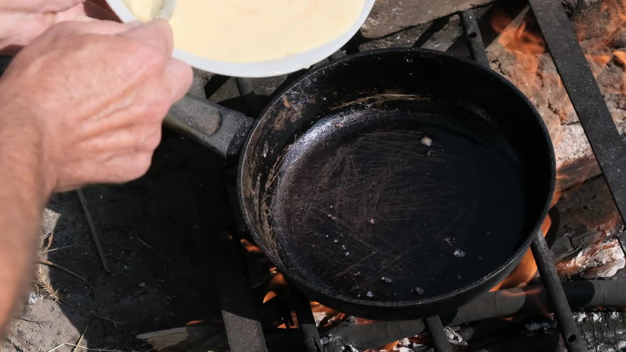 在野外用游客煎锅在篝火上烹饪煎蛋卷，慢动作视频素材