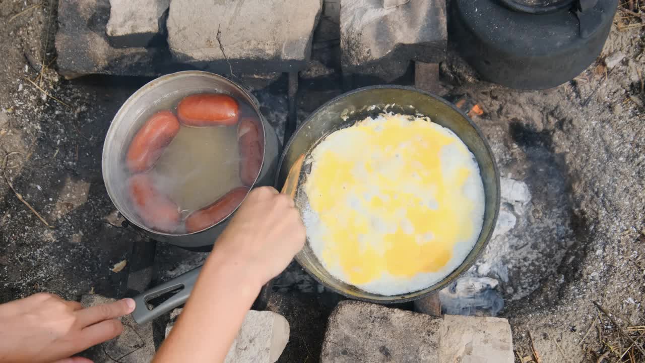 在野外用旅游煎锅在营火上煮炒鸡蛋和香肠视频素材