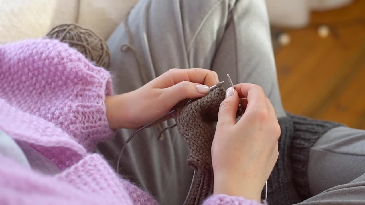 特写舒适的年轻女子编织针灰色袜子从天然羊毛线在冬天的时间在家里。视频素材