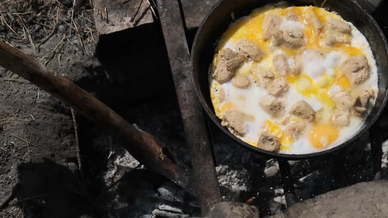 在旅游营火煎锅上煮炒蛋和鸡肉，自然视频素材