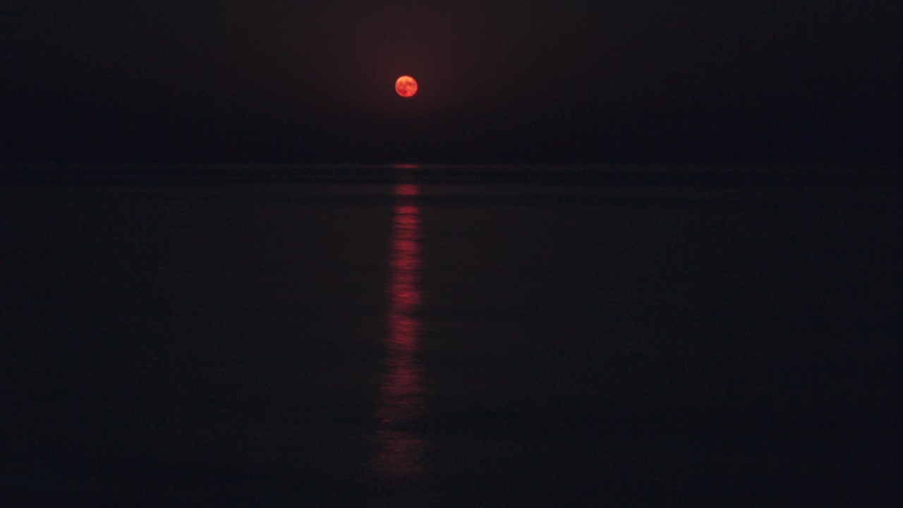 在一个黑暗的夜晚，平静的海面上，满月明亮地照耀着天空。水面上美丽的延时月亮之路视频素材