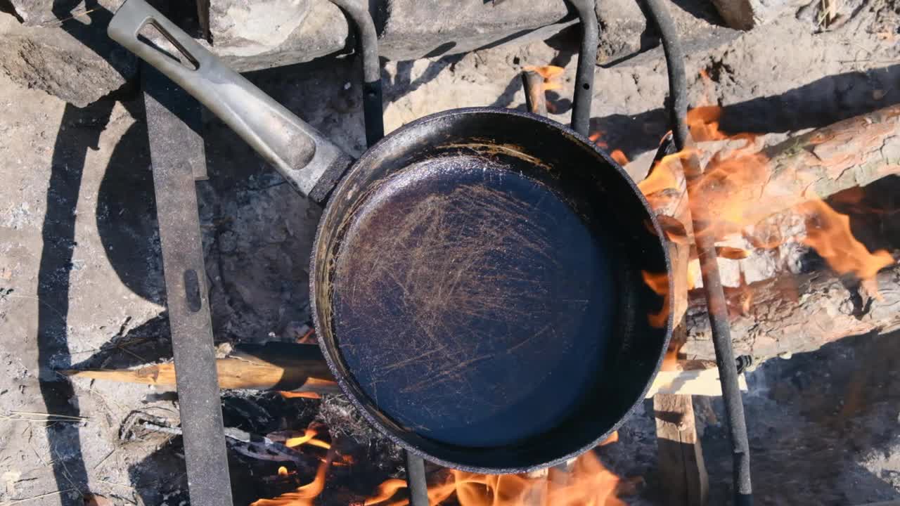 在野外用游客煎锅在篝火上烹饪煎蛋卷，慢动作视频素材