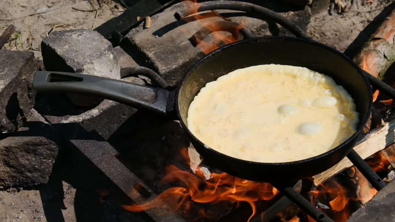 在野外用游客煎锅在篝火上烹饪煎蛋卷，慢动作视频素材