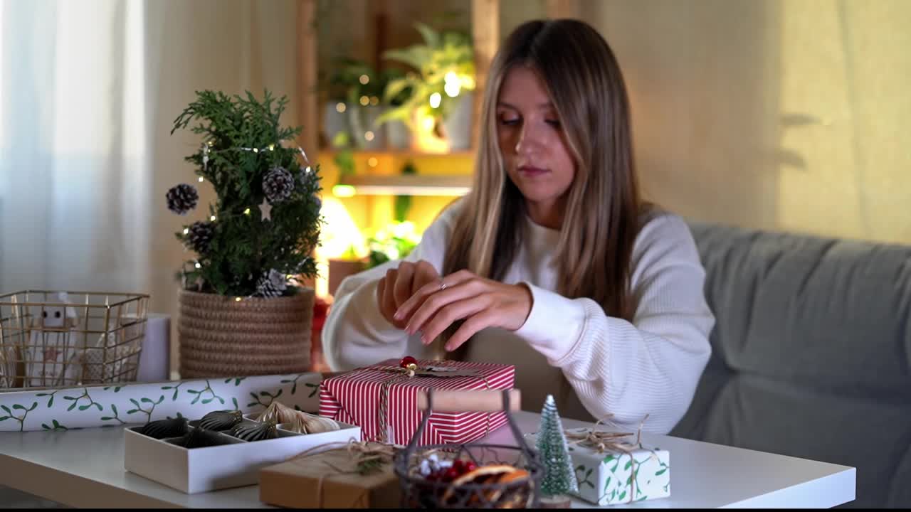 女人在家里包装圣诞节生态自然的礼品盒。准备礼物在白色的桌子上装饰元素，灯和物品圣诞节或新年DIY包装概念视频素材