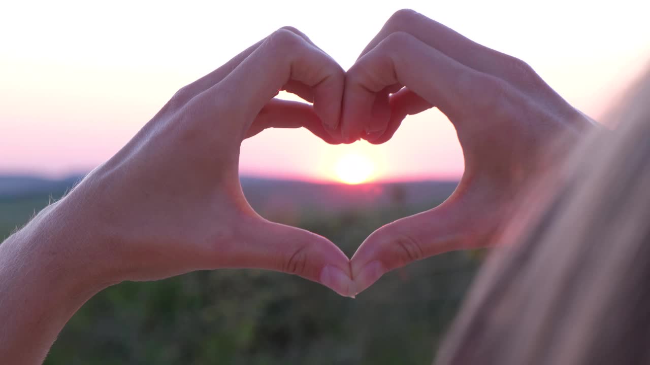 女性的手以心的形式对着天空通过夕阳的光束。手做成爱心的形状。视频素材