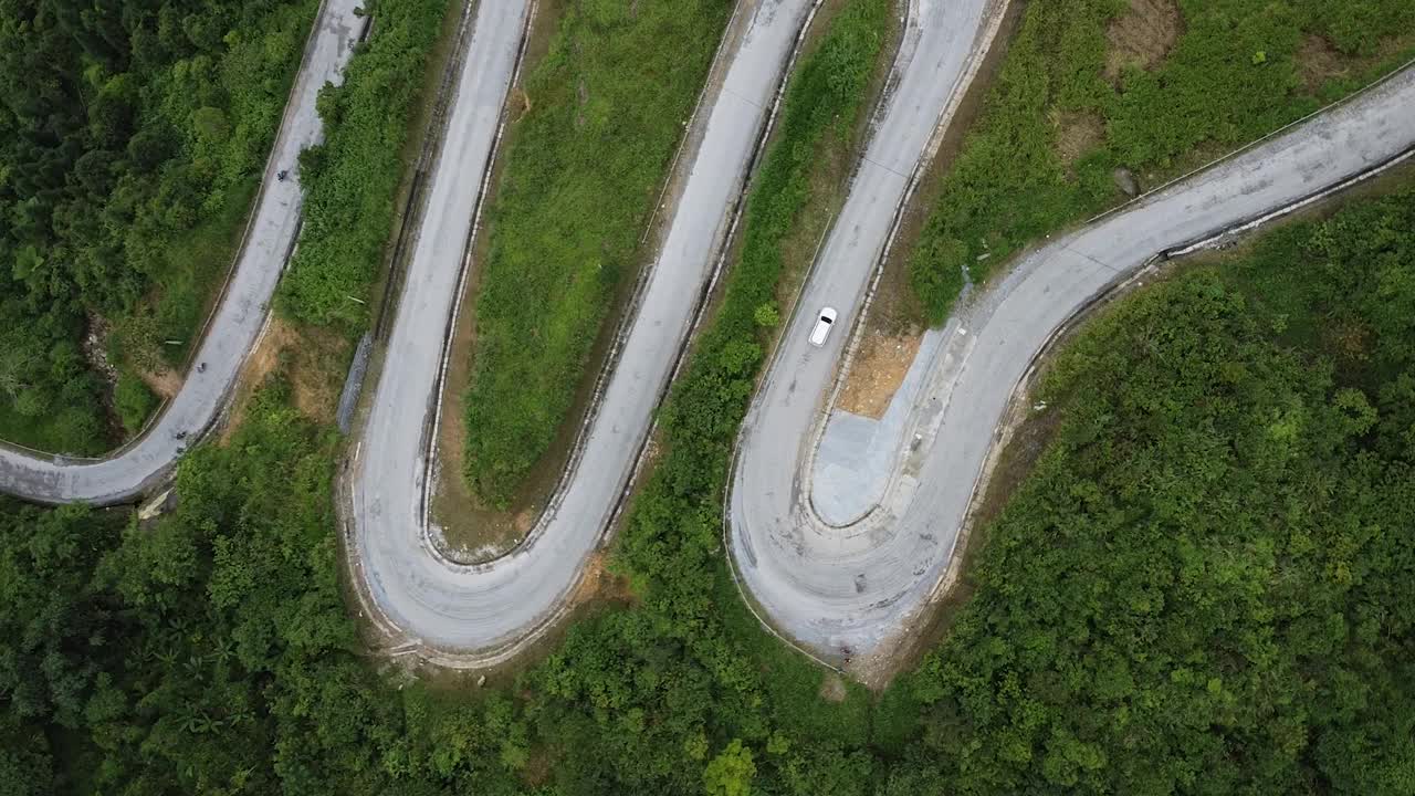 鸟瞰图在山中弯曲的道路，围绕一个绿色的森林和当地居民的住宅建筑视频素材