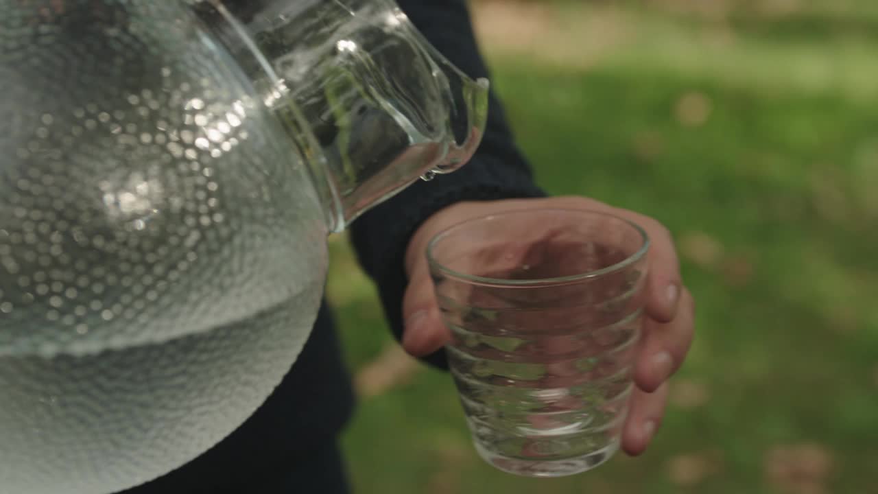 年轻的手把水从罐子里倒到杯子里，老而脏的手拿着杯子视频素材