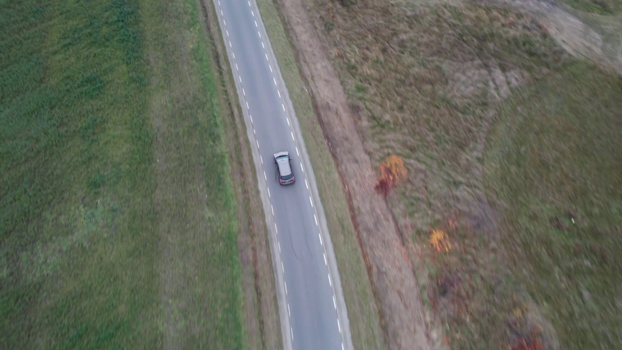 汽车正行驶在穿过田野的道路上，无人机拍下了鸟瞰图。秋天的时候在柏油路上，镜头跟着车走。视频素材