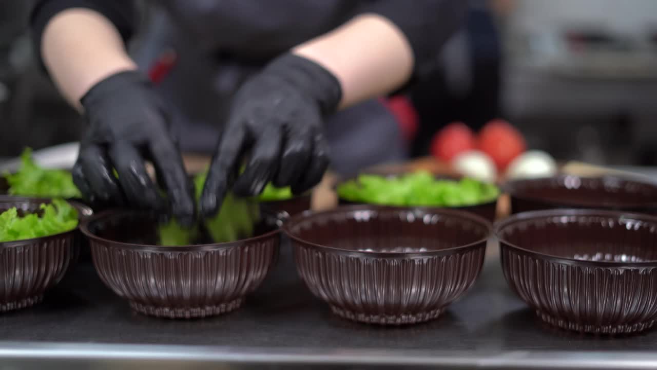 餐馆的外卖食品。厨师戴着手套的手的特写镜头把生菜叶子放进一个一次性塑料容器里，用来送食物。视频素材